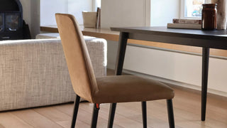 Lifestyle image of a cognac Mobitec Rob chair with black legs at a black table by a sofa