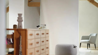 Lifestyle image of a grey Mobitec Thalia pouf and armchair in a bright attic room with chest of drawers