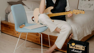 Lifestyle image of a light blue Mobitec Pamp chair in a bedroom with a guitarist