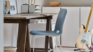 Lifestyle image of a blue Mobitec Pamp chair at a wooden table with guitar